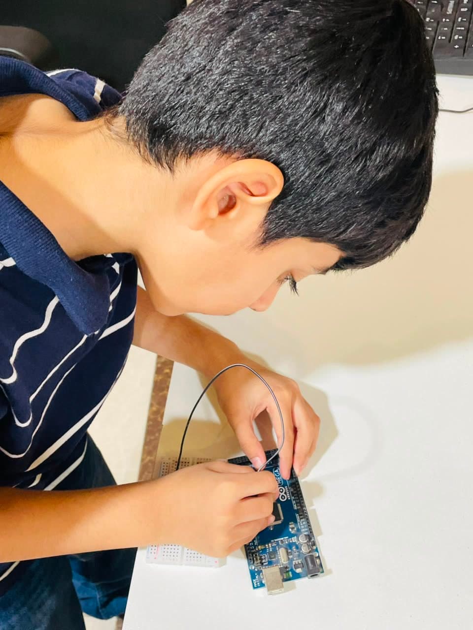 A student's hands connecting a wire to an Arduino Mega on the build table